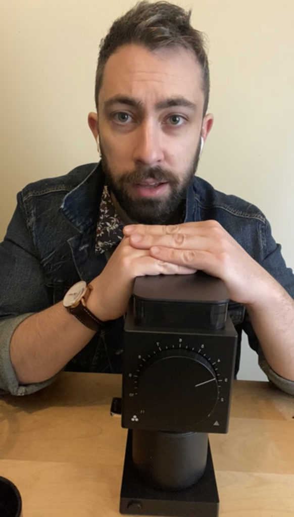 Matt, Hölbean Coffee Company's founder, sat at a desk, with his hands resting on the lid of a coffee grinder